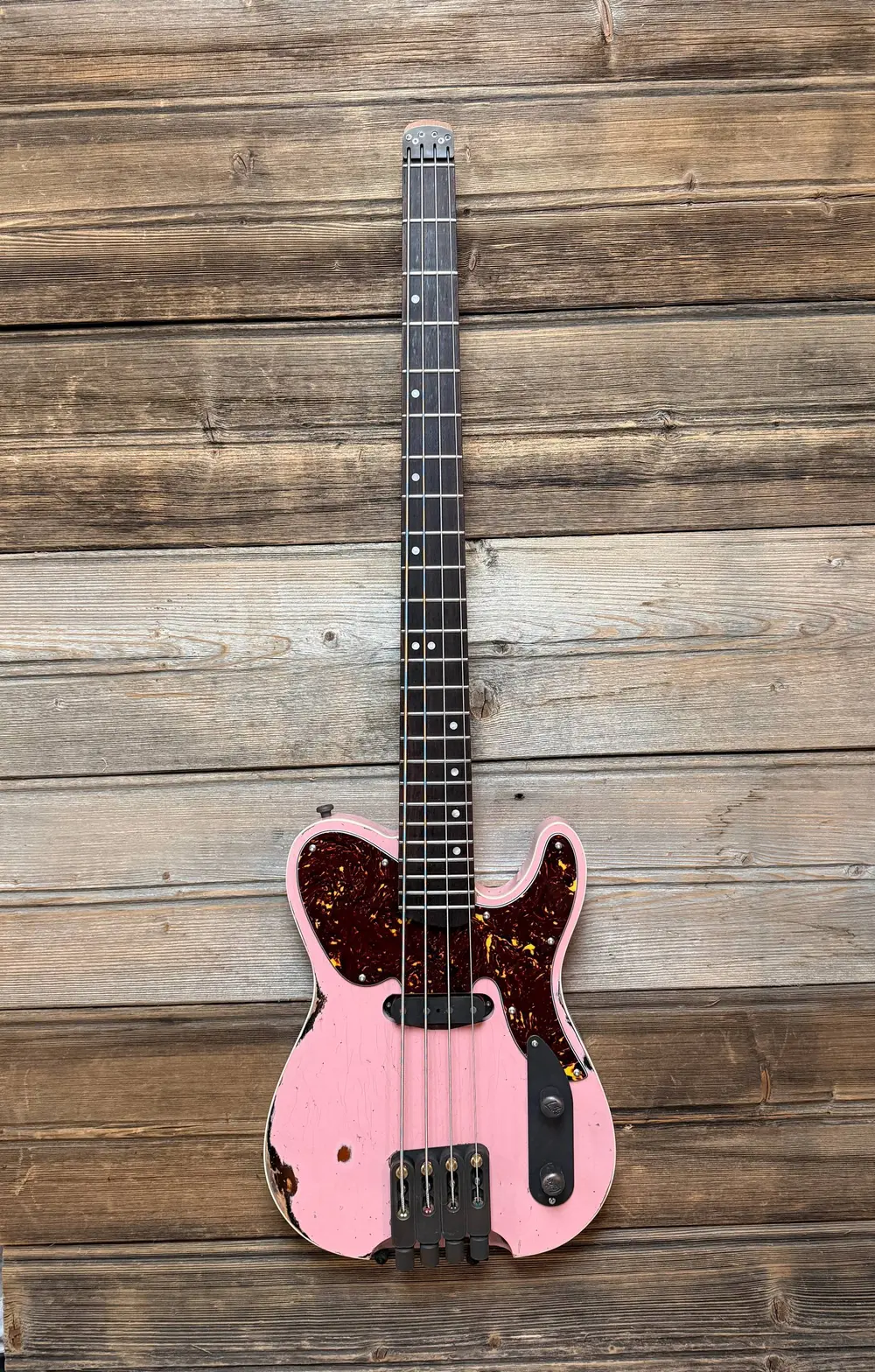 Custom Laika shell-pink relic single-cut bass with tortoiseshell guard and aged-brass hardware